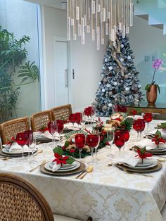 a dining room table set for christmas with red wine glasses and place settings on it