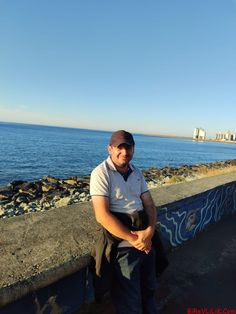 a man is sitting on the edge of a wall by the ocean with his arms crossed