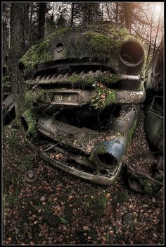 an old rusty car in the woods with moss growing out of it's hood