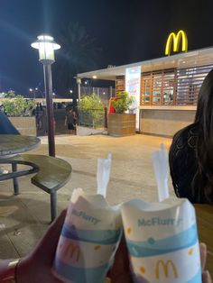 two mcdonald's drinks are sitting in front of a woman at a table outside