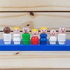 a group of small toy people sitting on top of a blue shelf next to a wooden wall