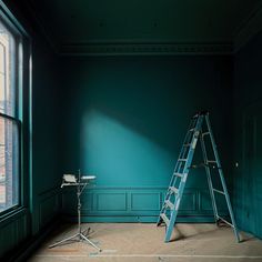 a ladder leaning against a wall in an empty room next to a window with blue paint