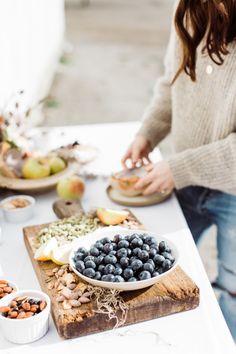 a woman standing at a table with plates of food on it and bowls of fruit in front of her