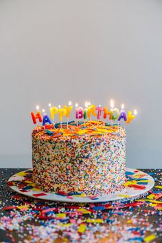 a birthday cake with lit candles sitting on top of a table covered in confetti and sprinkles