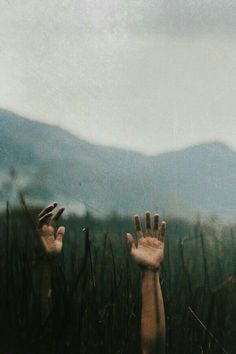 two hands reaching up into the air with mountains in the background