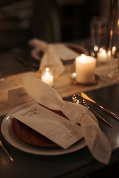 a white plate topped with a piece of cake on top of a table next to candles