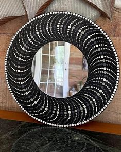 a decorative black and white circular mirror on a wooden table next to a bed with pillows