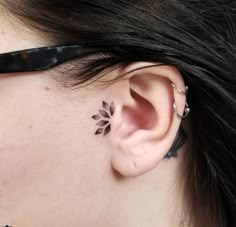 a woman's left ear has a small black flower tattoo on it