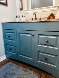 a bathroom vanity with blue cabinets and marble counter tops, along with a rug on the floor