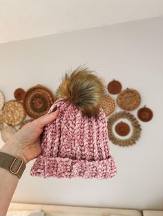 a hand holding a pink knitted hat in front of a wall