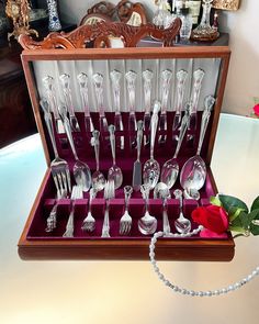 an assortment of silverware in a wooden box on a table next to a rose