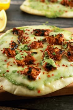 two pizzas sitting on top of a wooden cutting board next to lemon wedges