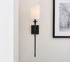 a wall mounted light with a white shade on it's side next to a framed photograph