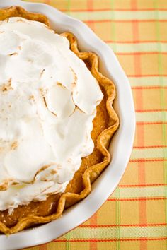 a pie with whipped cream on top in a white dish sitting on a colorful table cloth