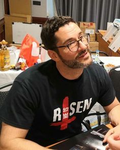 a man sitting at a table with a book in his hand and looking off to the side