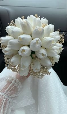 a bouquet of white tulips and baby's breath sits in the passenger seat of a car