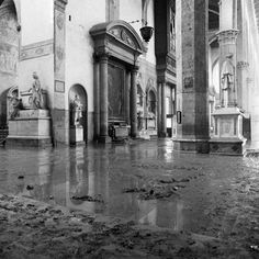 black and white photograph of the inside of a building with rain on the ground in front of it