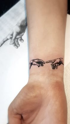 two hands touching each other with the creation of man's hand tattoo on wrist