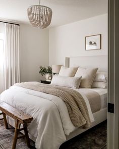 a white bed sitting next to a wooden bench in a bedroom under a chandelier