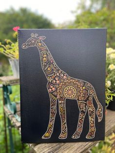 a giraffe painted on a black canvas sitting on a wooden table next to flowers