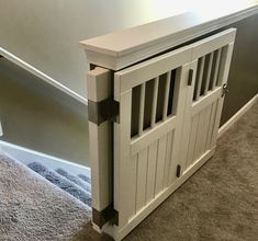 a white dog crate sitting on top of carpeted floor next to a stair case