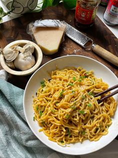 a white bowl filled with noodles next to garlic and cloves on a wooden table