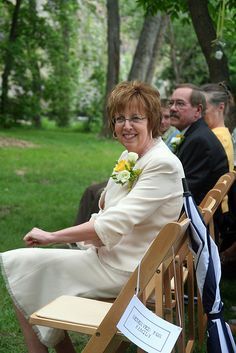 an older woman sitting on a wooden bench in front of other people at a wedding