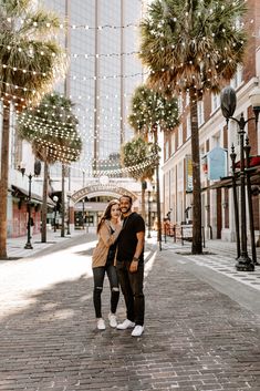 a man and woman standing in the middle of an empty street with palm trees on both sides