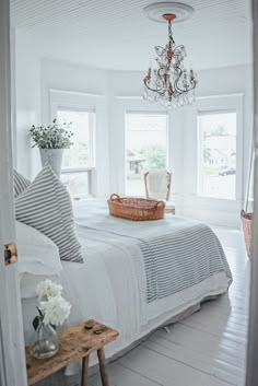 a white bedroom with a chandelier hanging from the ceiling and pillows on the bed