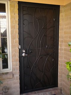 a black door with vines on it in front of a brick wall and planter