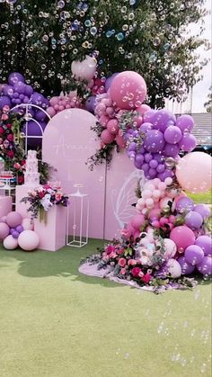 an outdoor party with balloons and flowers on the ground, in front of a pink wall