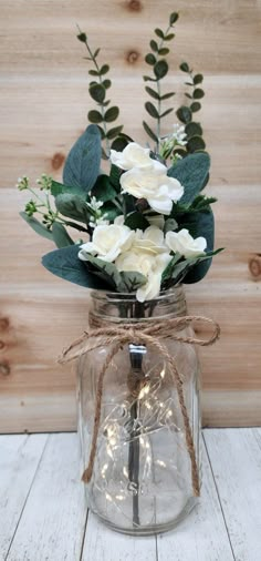 a glass jar filled with white flowers and greenery