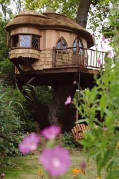 a tree house built into the side of a lush green forest with purple flowers in the foreground