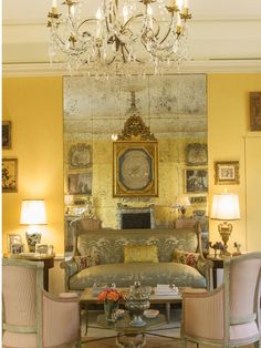 a living room filled with furniture and a chandelier hanging from the ceiling in front of a mirror