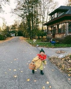 a young child dressed as a scarecrow carrying a basket in front of a house