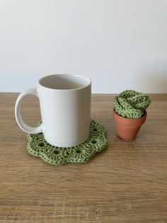 two crocheted coasters sit next to a coffee cup on a wooden table