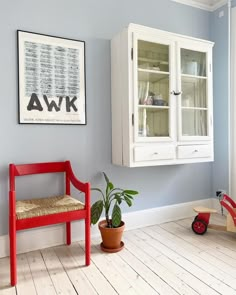 a red chair sitting next to a white cabinet on top of a hard wood floor