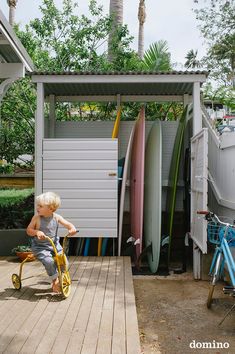 a young boy pushing a tricycle through a yard with lots of surfboards on it