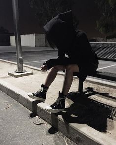 a person sitting on a bench with their head in his hands, wearing black hoodie and sneakers