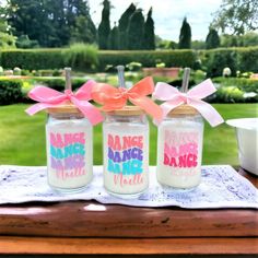 three mason jars with pink and blue writing on them sitting on a table in front of a garden