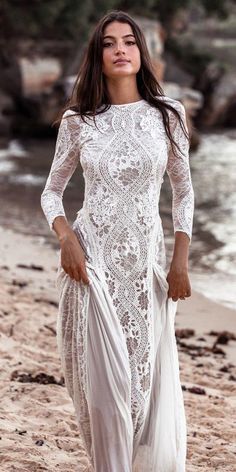 a woman walking on the beach wearing a white dress with sheer sleeves and an open back