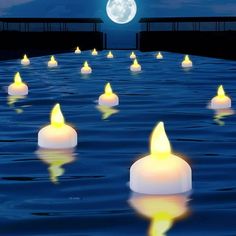 many lit candles floating in the water with a full moon in the sky behind them