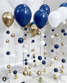 blue, white and gold balloons are hanging from the ceiling in a room with marble flooring