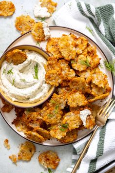 a white plate topped with fried food next to a bowl of ranch dressing and a fork