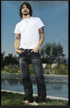 a man standing in the grass with his hands in his pockets and wearing a white t - shirt