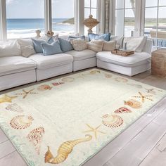 a living room filled with lots of white furniture and large windows next to the ocean