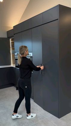 a woman in black shirt and leggings opening the door to a gray kitchen