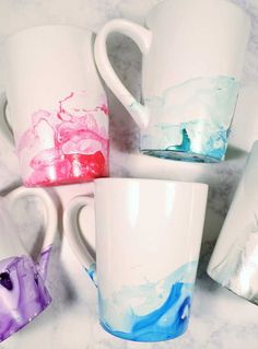 four coffee mugs painted with different colors and shapes, sitting on a marble surface