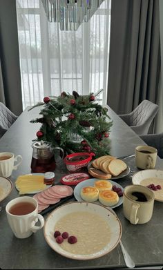 a table topped with plates and bowls filled with food next to a potted christmas tree