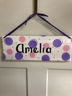 a door hanger with the word ameli painted on it and purple, pink and green polka dots